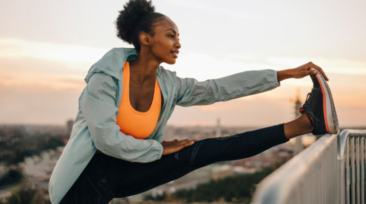 Woman in athletic clothes stretching her leg on a railing